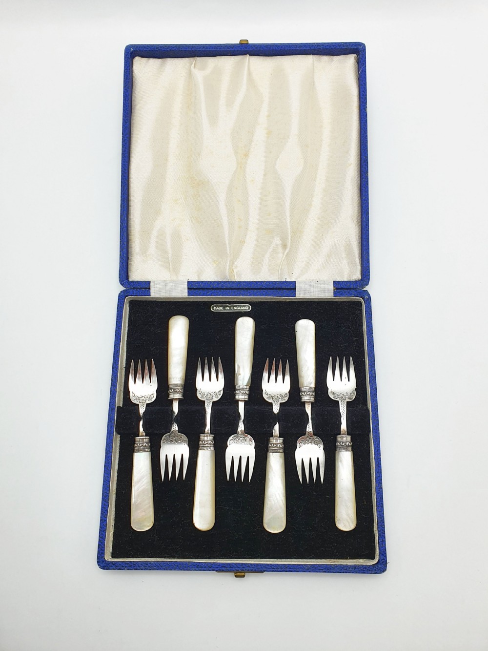 A cased set of six Victorian hors doeuvres forks featuring mother-of-pearl handles and engraved silver-plated tines, presented in a blue fabric-lined box.