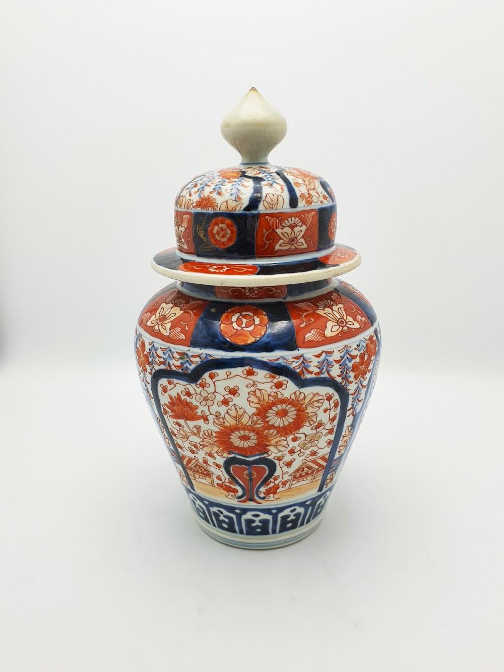 A Japanese Imari porcelain covered ginger jar decorated with hand-painted iron-red and cobalt-blue floral panels, complete with a domed lid and pointed finial. View II