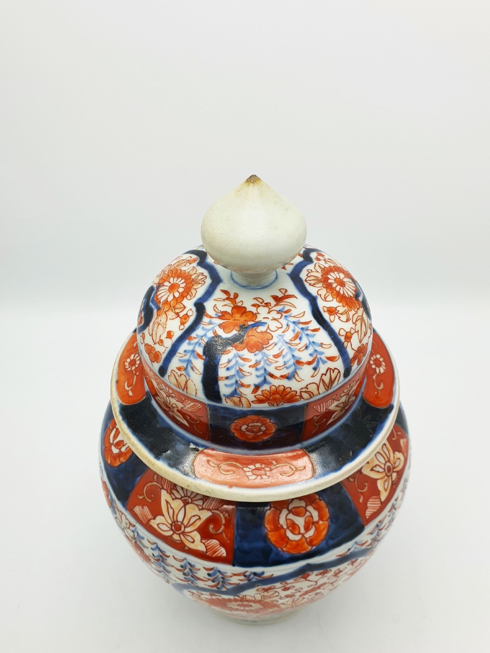 A Japanese Imari porcelain covered ginger jar decorated with hand-painted iron-red and cobalt-blue floral panels, complete with a domed lid and pointed finial. View V