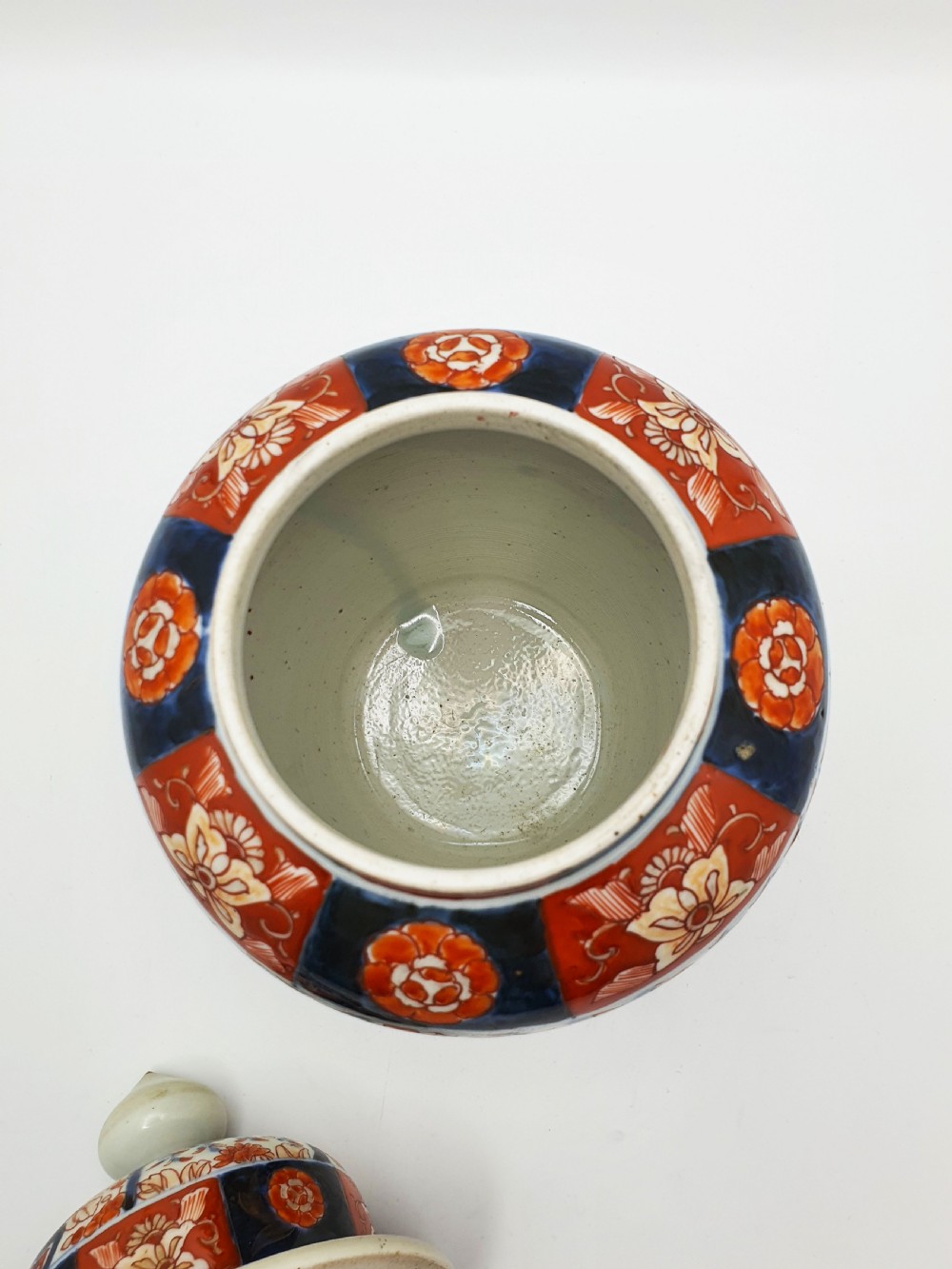 A Japanese Imari porcelain covered ginger jar decorated with hand-painted iron-red and cobalt-blue floral panels, complete with a domed lid and pointed finial. View VI