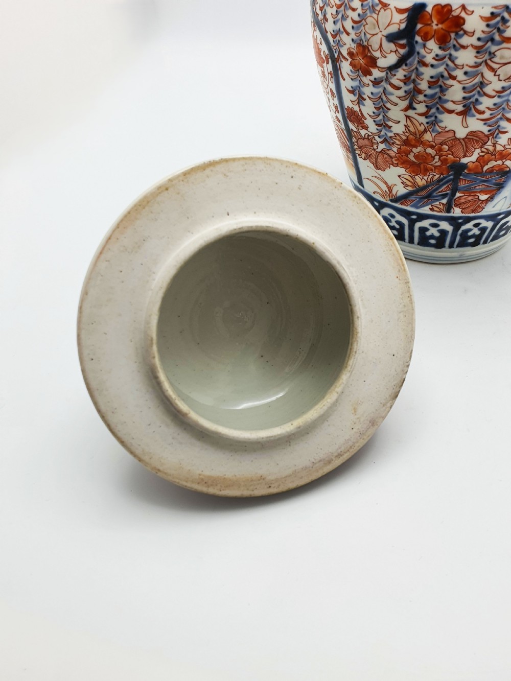 A Japanese Imari porcelain covered ginger jar decorated with hand-painted iron-red and cobalt-blue floral panels, complete with a domed lid and pointed finial. View VII