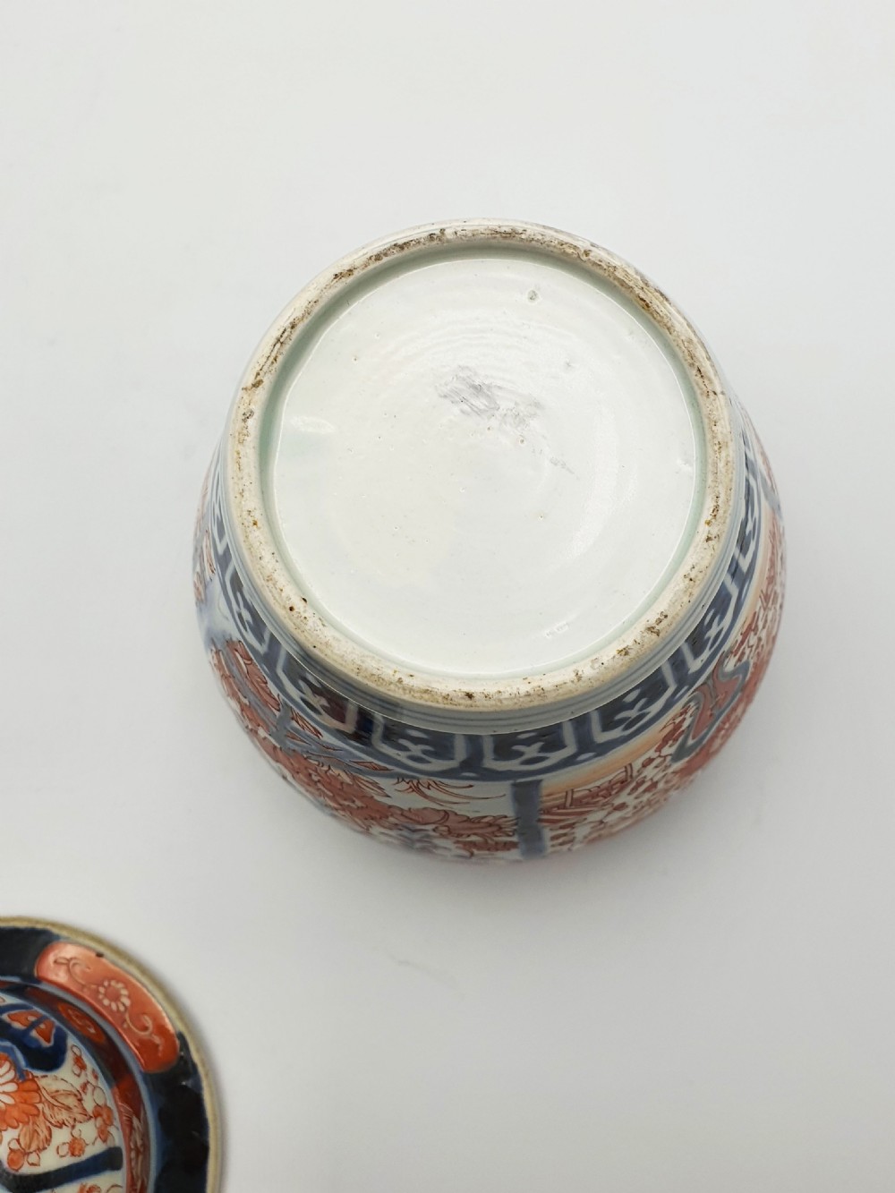 A Japanese Imari porcelain covered ginger jar decorated with hand-painted iron-red and cobalt-blue floral panels, complete with a domed lid and pointed finial. View VIII