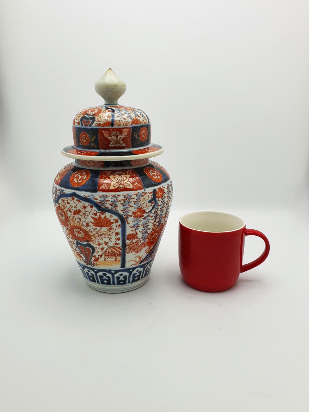 A Japanese Imari porcelain covered ginger jar decorated with hand-painted iron-red and cobalt-blue floral panels, complete with a domed lid and pointed finial. View X