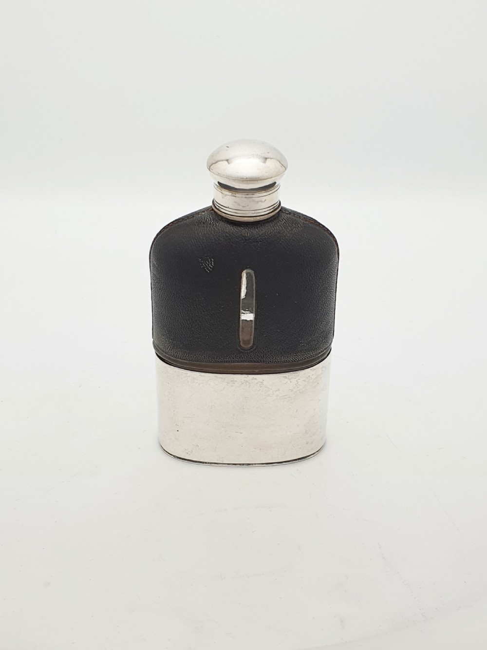 An Edwardian hip flask featuring a dark brown textured leather sleeve with a sight window, a removable silver-plated base cup, and a rounded silver-plated cap.