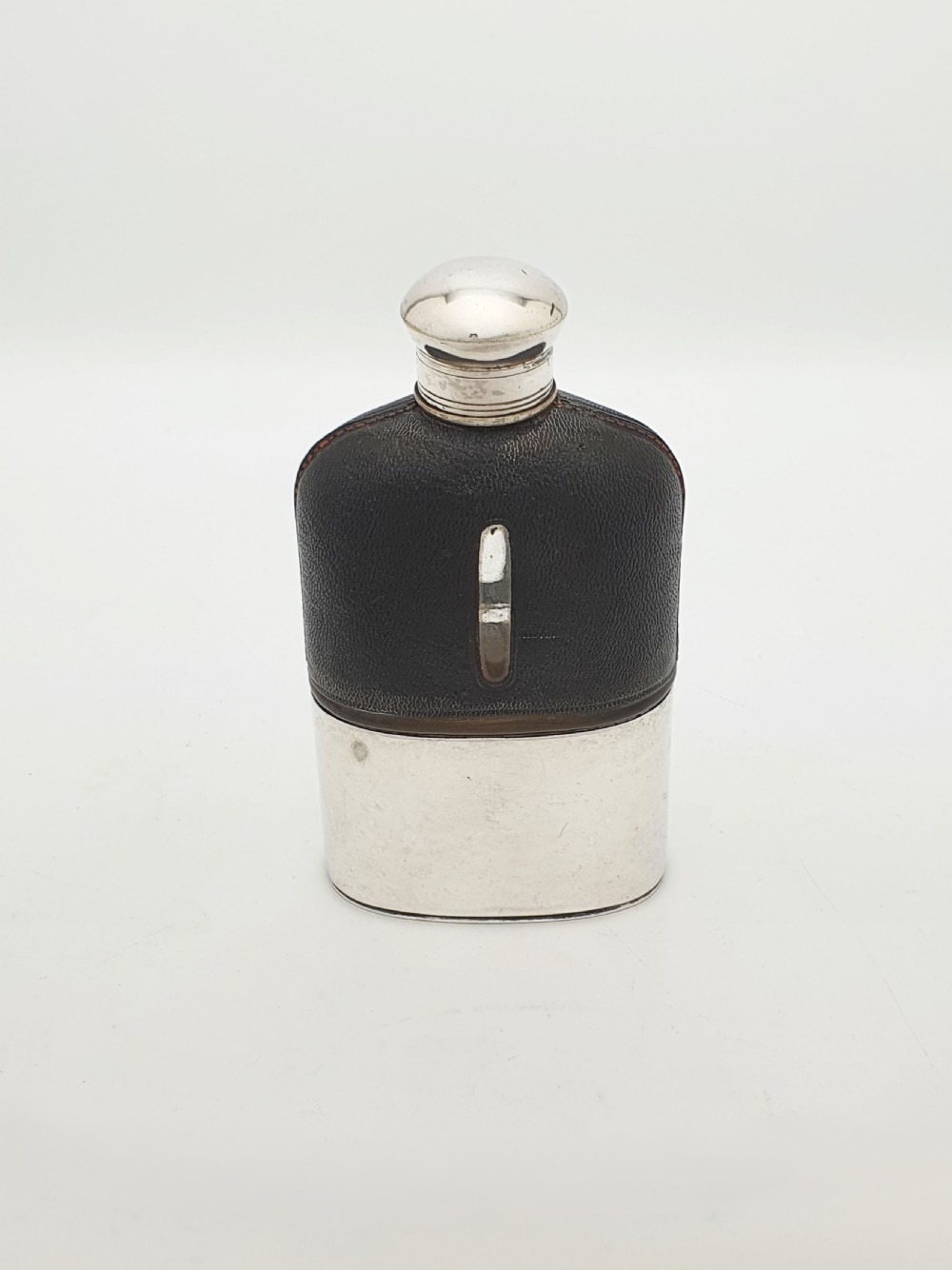 An Edwardian hip flask featuring a dark brown textured leather sleeve with a sight window, a removable silver-plated base cup, and a rounded silver-plated cap. View II