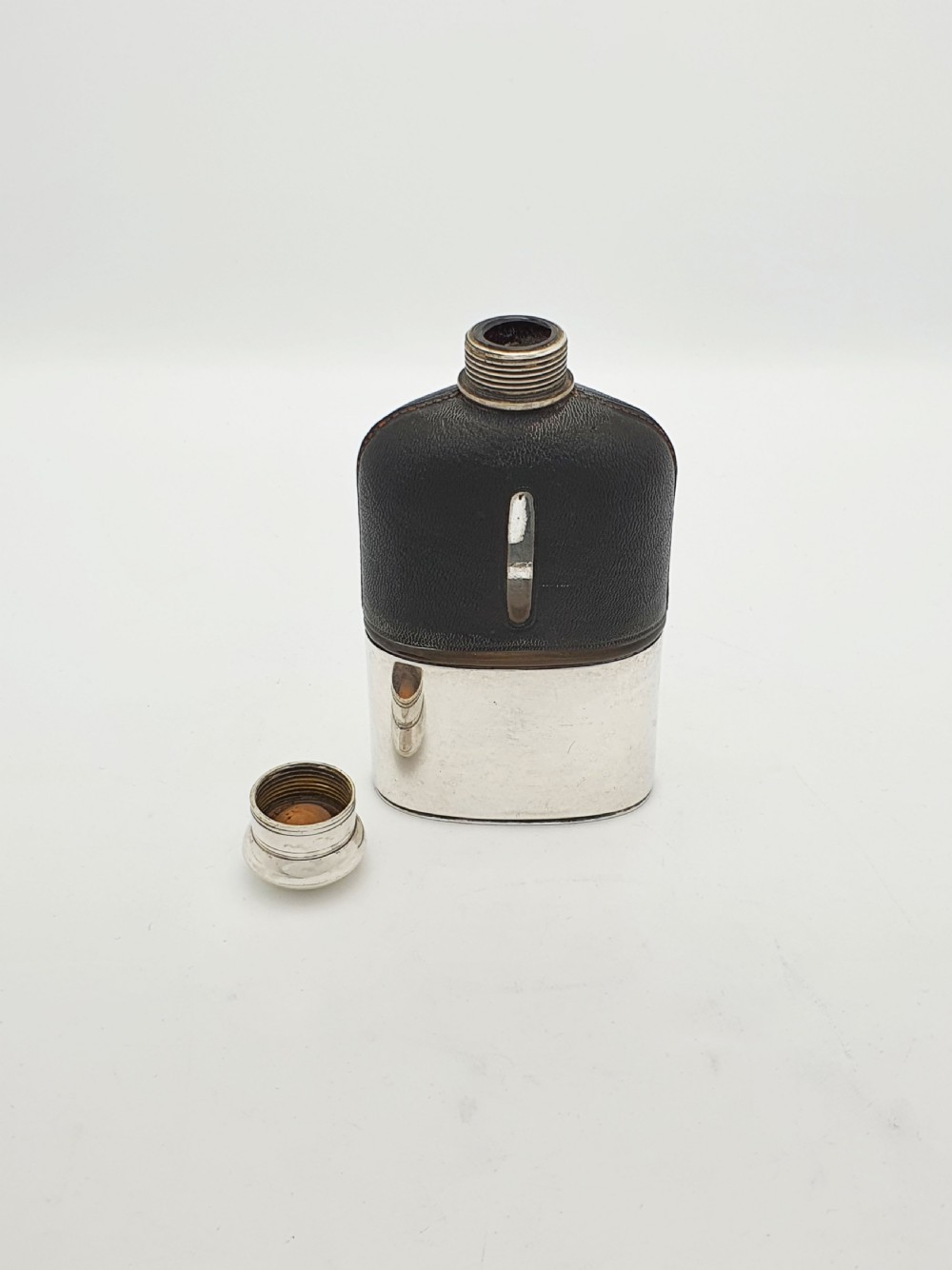 An Edwardian hip flask featuring a dark brown textured leather sleeve with a sight window, a removable silver-plated base cup, and a rounded silver-plated cap. View III