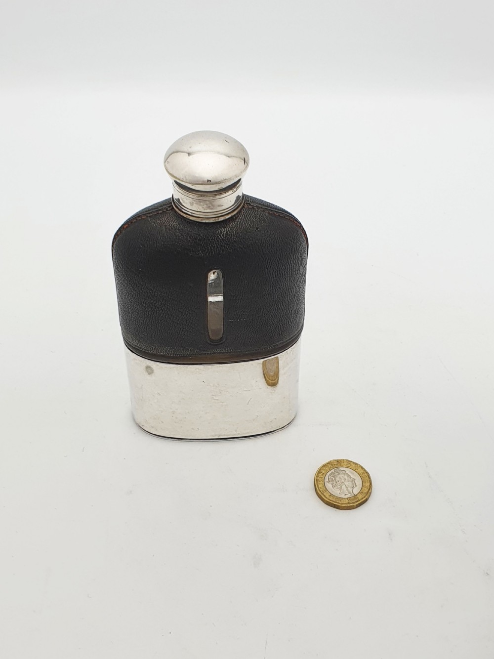 An Edwardian hip flask featuring a dark brown textured leather sleeve with a sight window, a removable silver-plated base cup, and a rounded silver-plated cap. View VIII