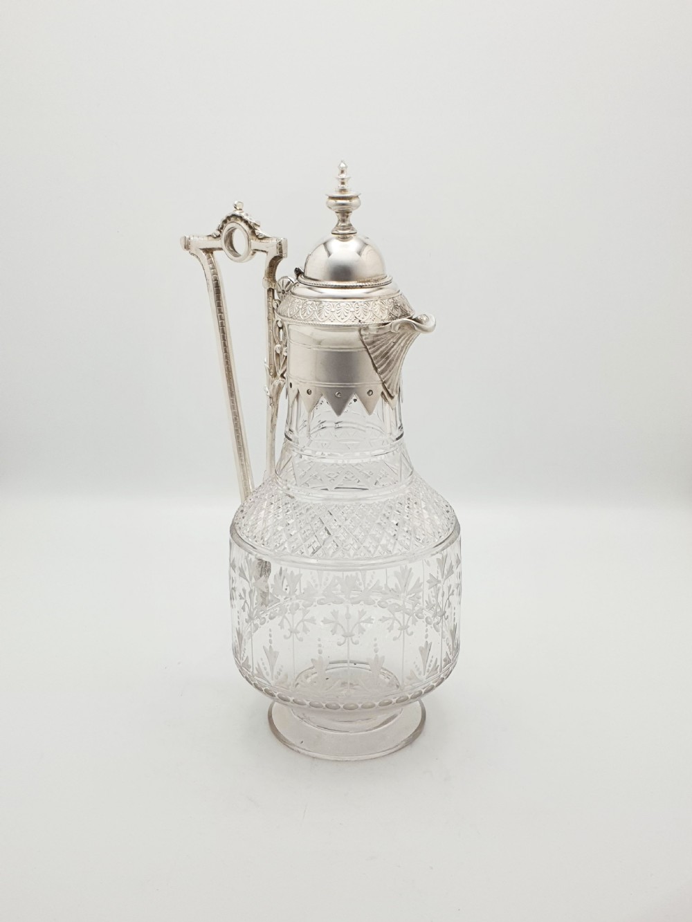A late Victorian silver-plated and clear cut-glass claret jug with an engraved foliate body, domed hinged lid, and decorative angular handle. View III
