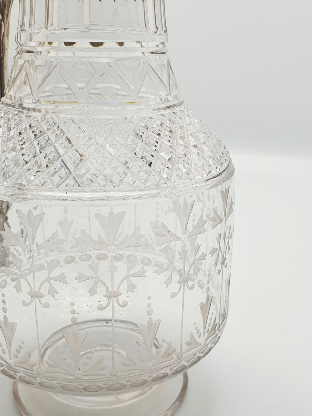 A late Victorian silver-plated and clear cut-glass claret jug with an engraved foliate body, domed hinged lid, and decorative angular handle. View VII