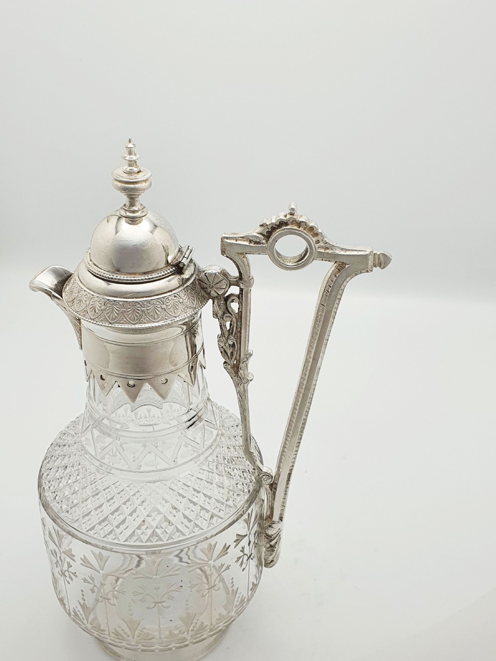 A late Victorian silver-plated and clear cut-glass claret jug with an engraved foliate body, domed hinged lid, and decorative angular handle. View VIII