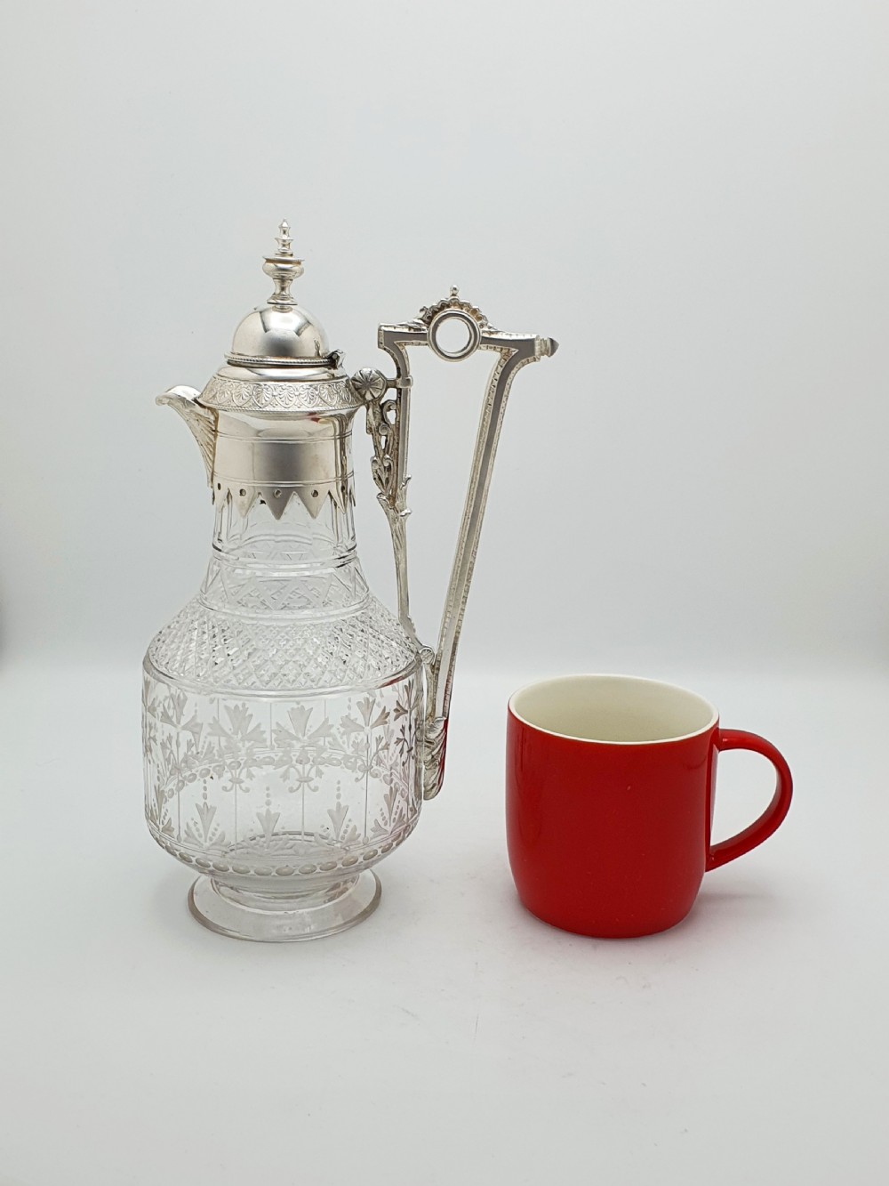 A late Victorian silver-plated and clear cut-glass claret jug with an engraved foliate body, domed hinged lid, and decorative angular handle. View IX