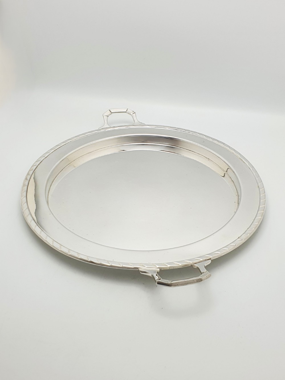 A circular Art Deco silver-plated serving tray featuring angular geometric handles and a simple raised border.