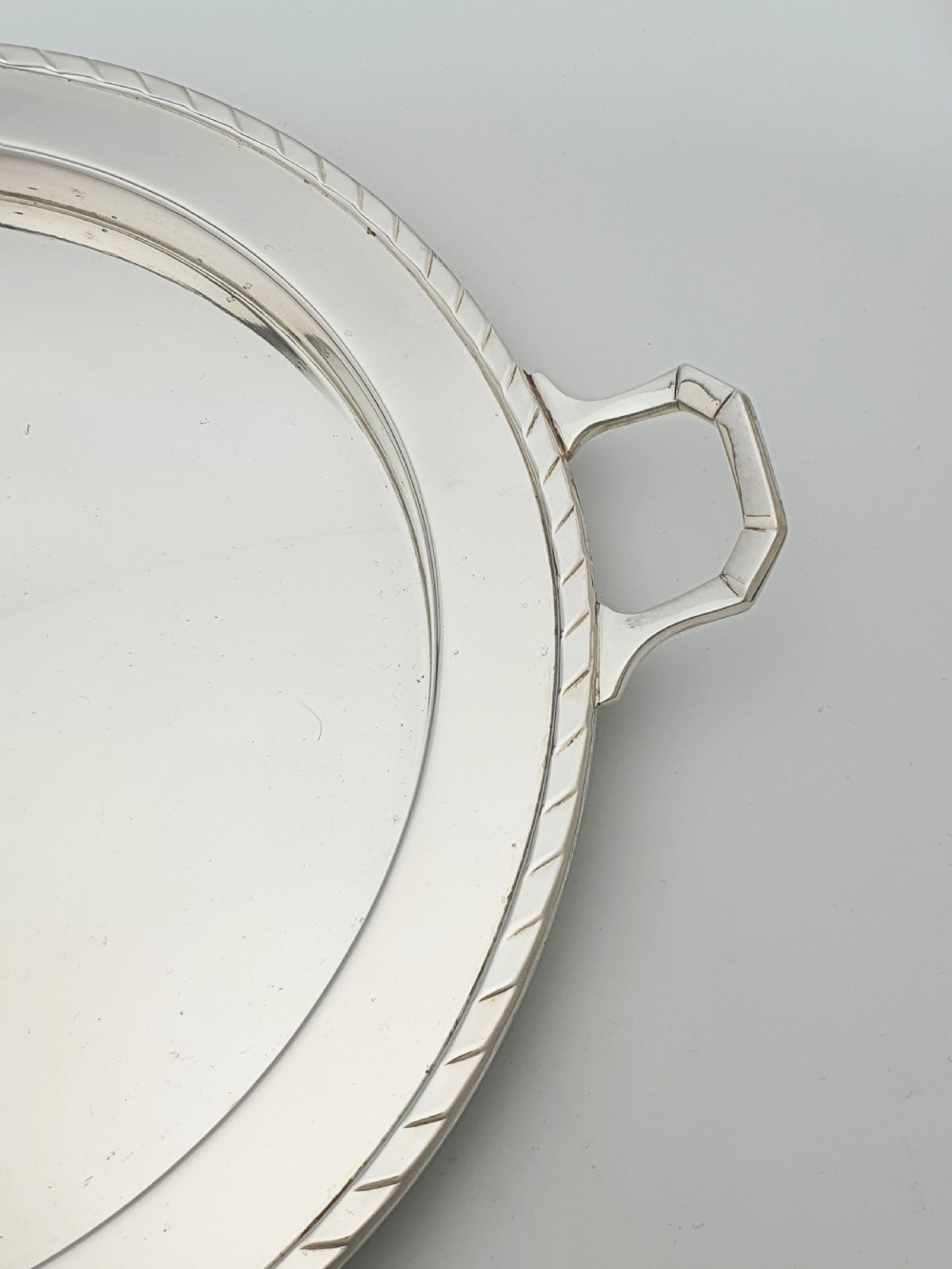 A circular Art Deco silver-plated serving tray featuring angular geometric handles and a simple raised border. View II