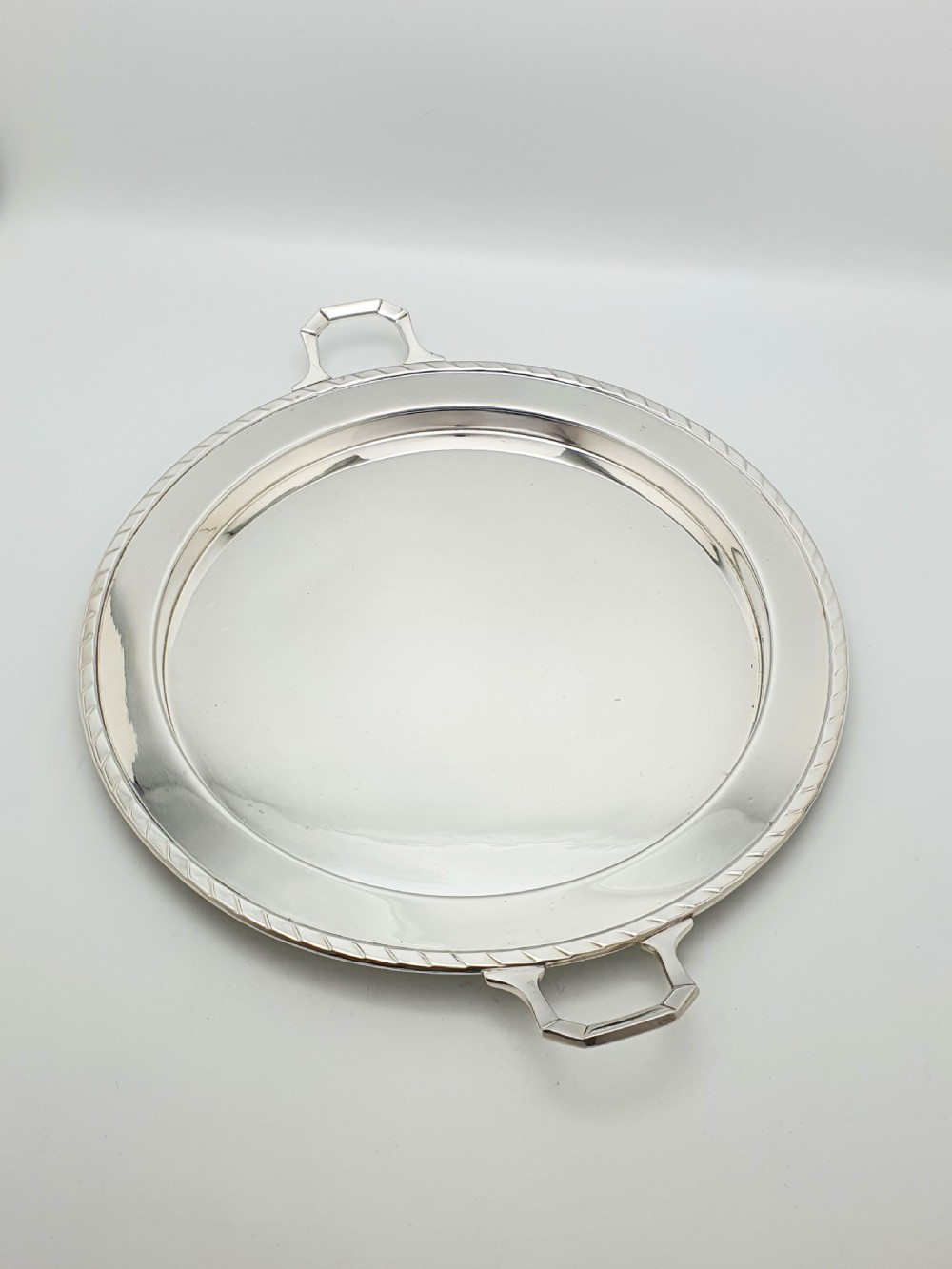 A circular Art Deco silver-plated serving tray featuring angular geometric handles and a simple raised border. View V