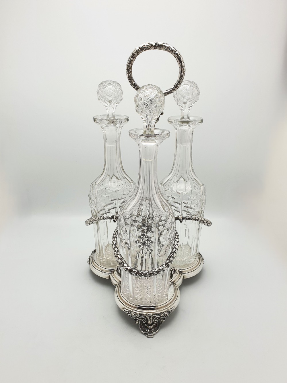 A Victorian silver-plated three-bottle decanter stand holding three clear cut-glass decanters with matching stoppers.