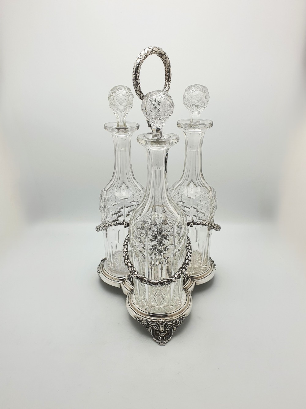 A Victorian silver-plated three-bottle decanter stand holding three clear cut-glass decanters with matching stoppers. View II
