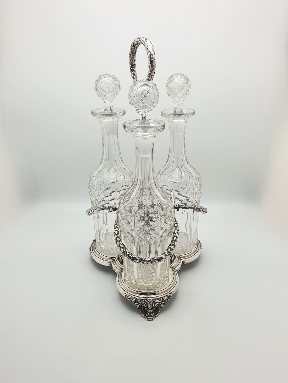 A Victorian silver-plated three-bottle decanter stand holding three clear cut-glass decanters with matching stoppers. View III