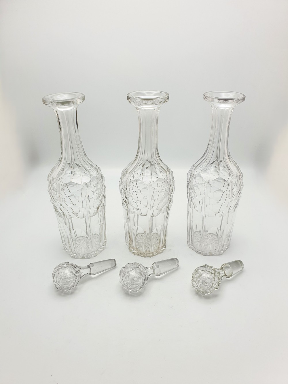 A Victorian silver-plated three-bottle decanter stand holding three clear cut-glass decanters with matching stoppers. View VIII