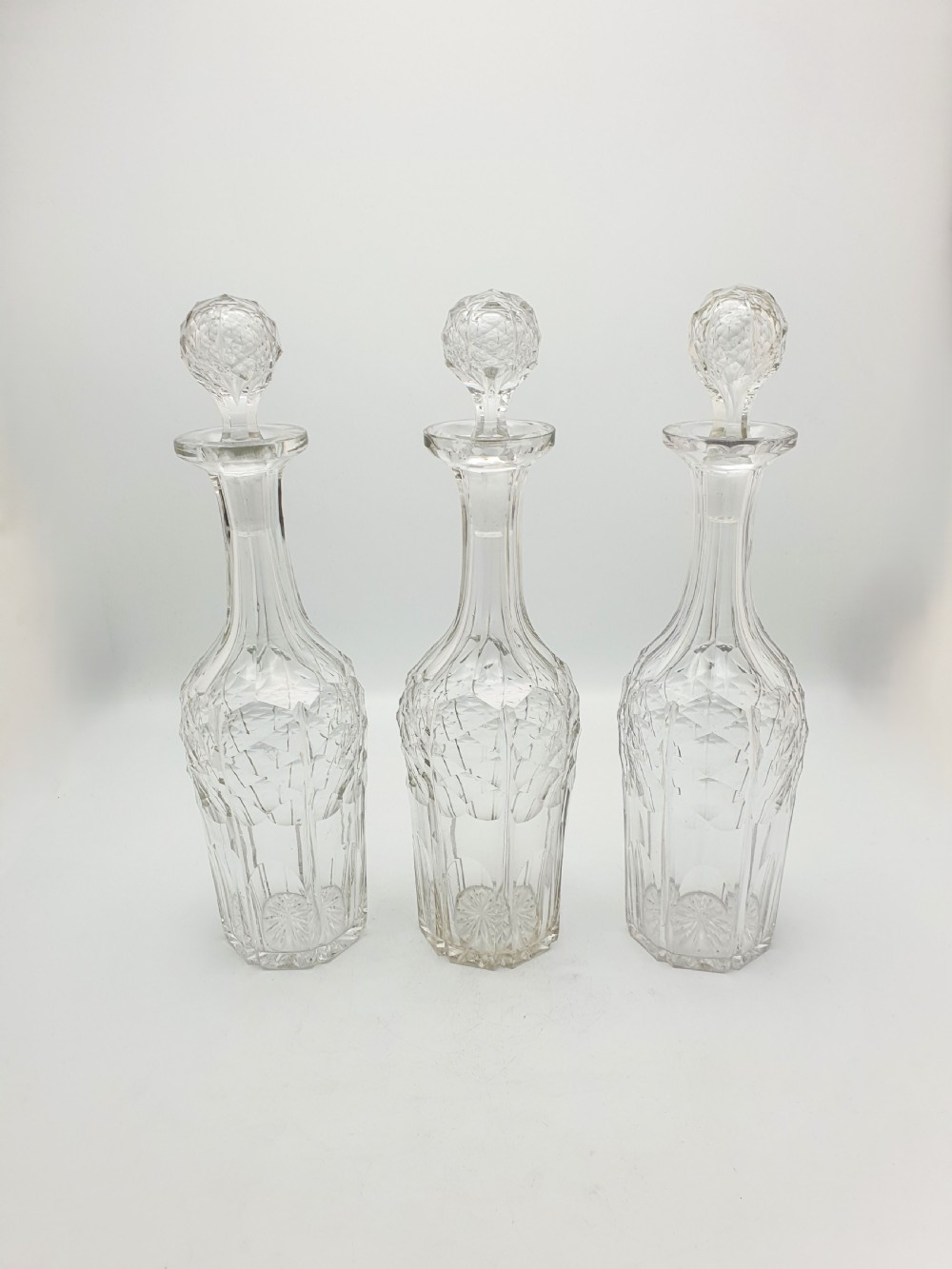 A Victorian silver-plated three-bottle decanter stand holding three clear cut-glass decanters with matching stoppers. View IX