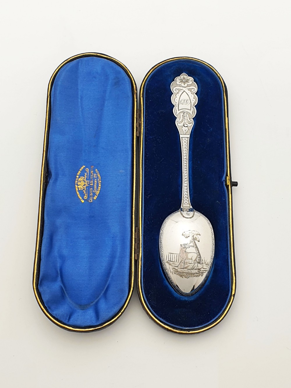 An 1877 Victorian sterling silver presentation spoon with an engraved stag motif inside an open blue velvet presentation box.