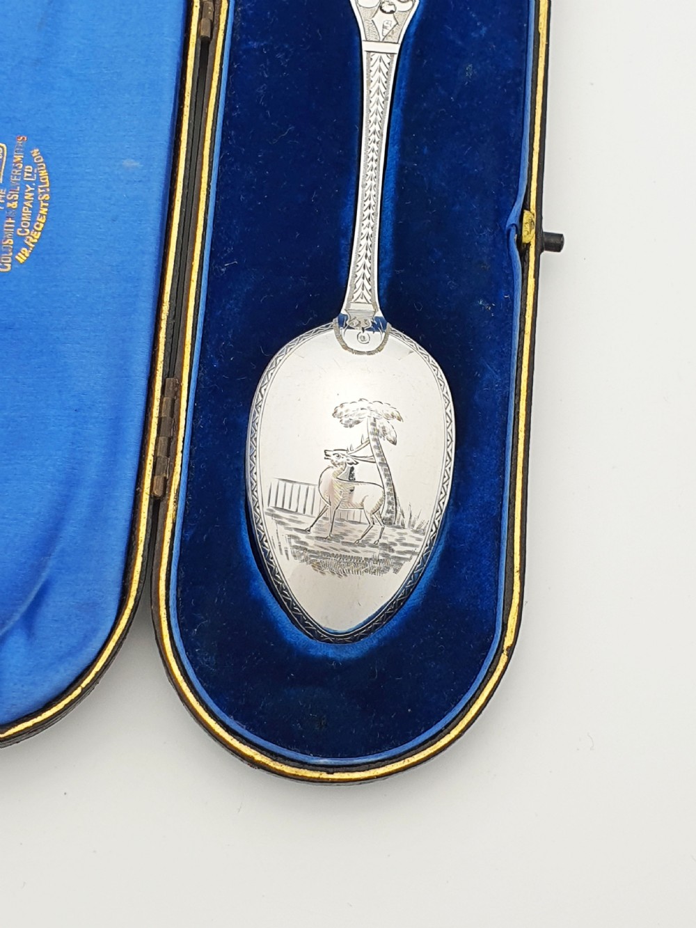 An 1877 Victorian sterling silver presentation spoon with an engraved stag motif inside an open blue velvet presentation box. View II