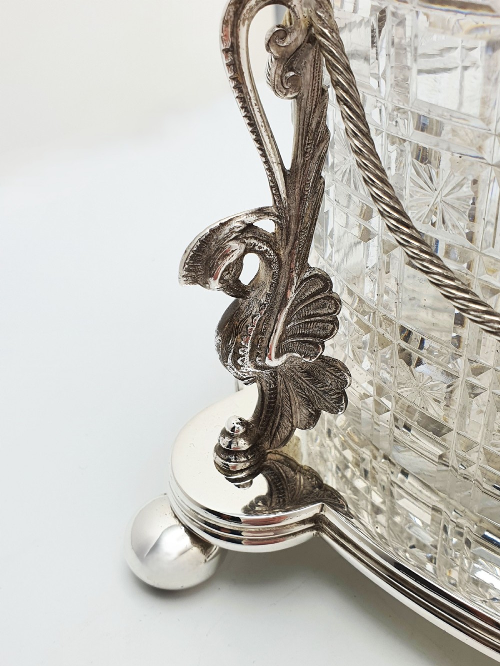 An oval cut crystal biscuit barrel featuring silver-plated mounts, ball feet, twisted rope swags, and an engraved lid topped with a heraldic dragon finial. View III