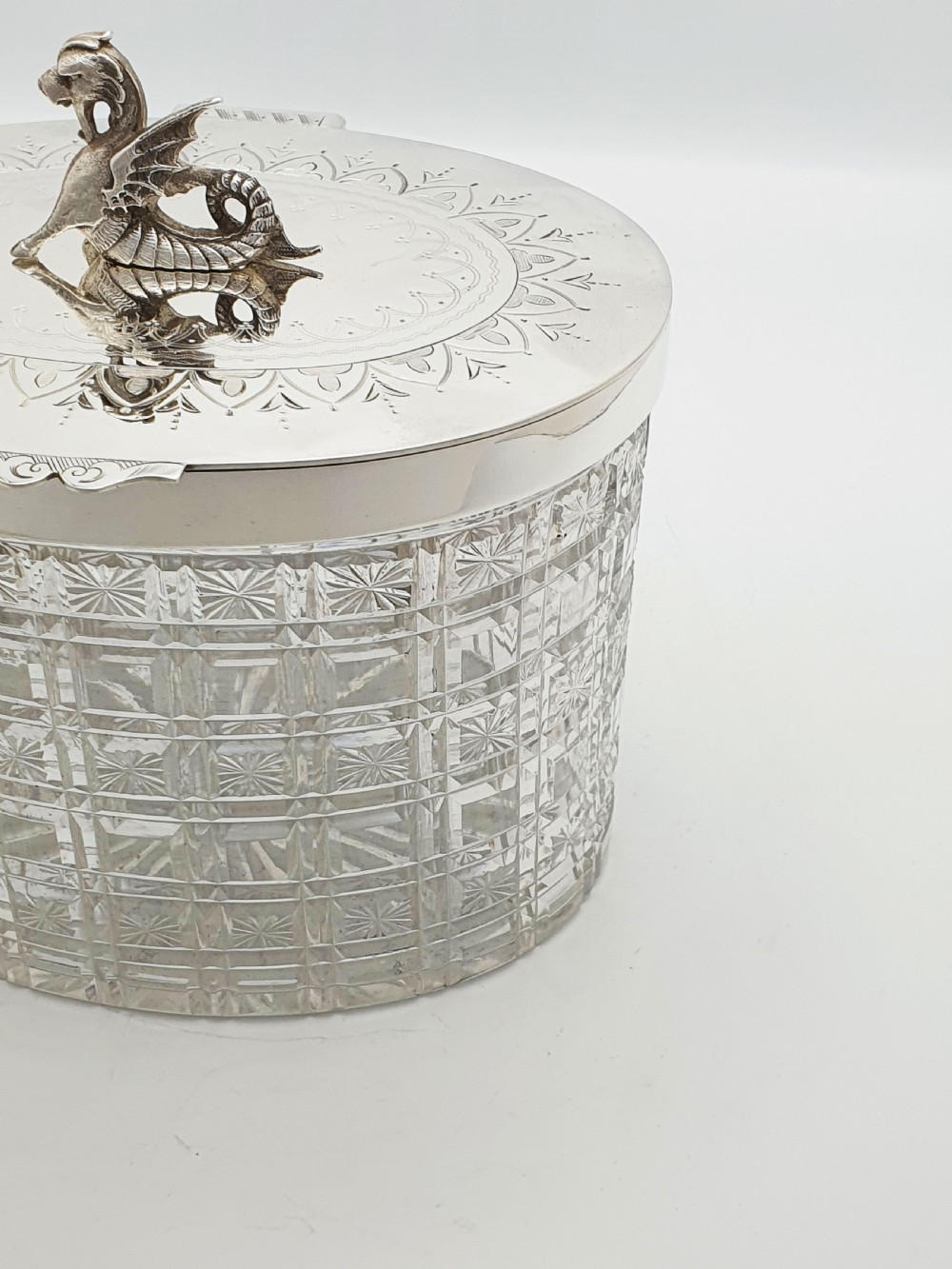 An oval cut crystal biscuit barrel featuring silver-plated mounts, ball feet, twisted rope swags, and an engraved lid topped with a heraldic dragon finial. View XIII