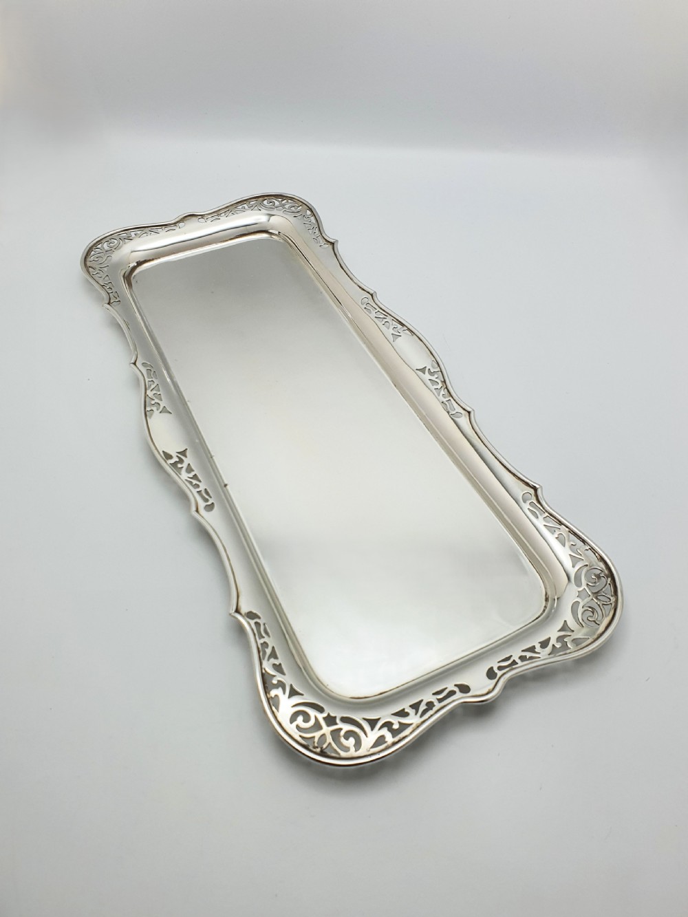 A rectangular silver-plated cocktail tray featuring a pierced scrollwork border and a smooth reflective centre.