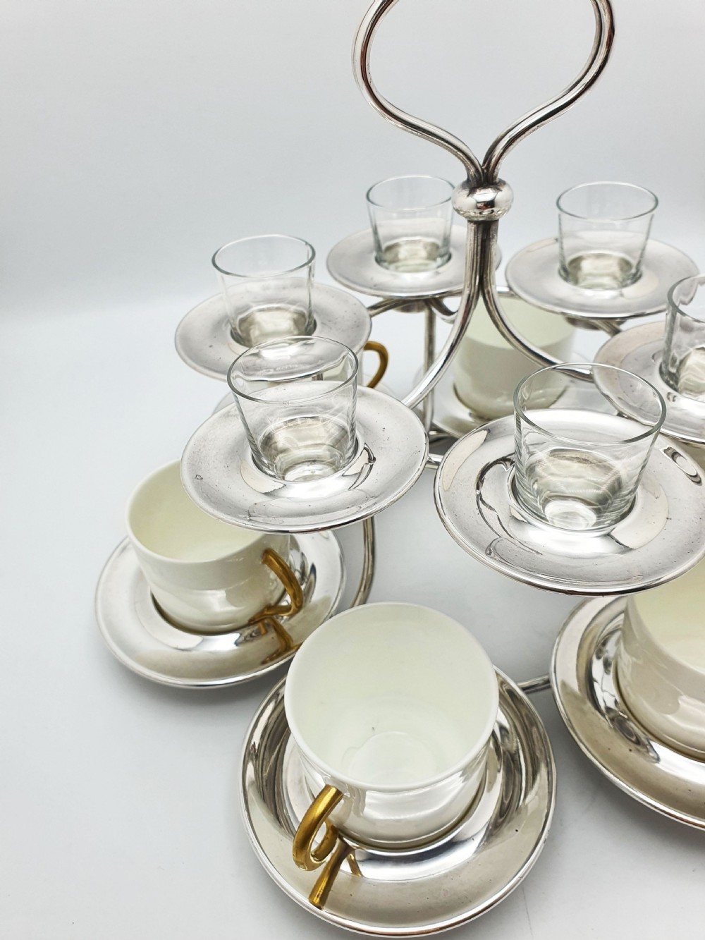 A silver-plated tiered service stand holding six cream ceramic demitasse cups on the lower level and six glass liqueur cups above. View III