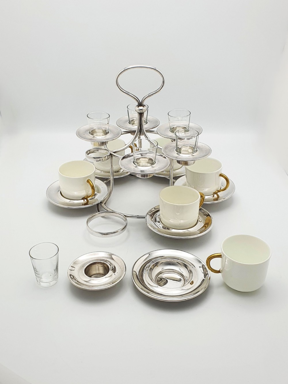 A silver-plated tiered service stand holding six cream ceramic demitasse cups on the lower level and six glass liqueur cups above. View VII