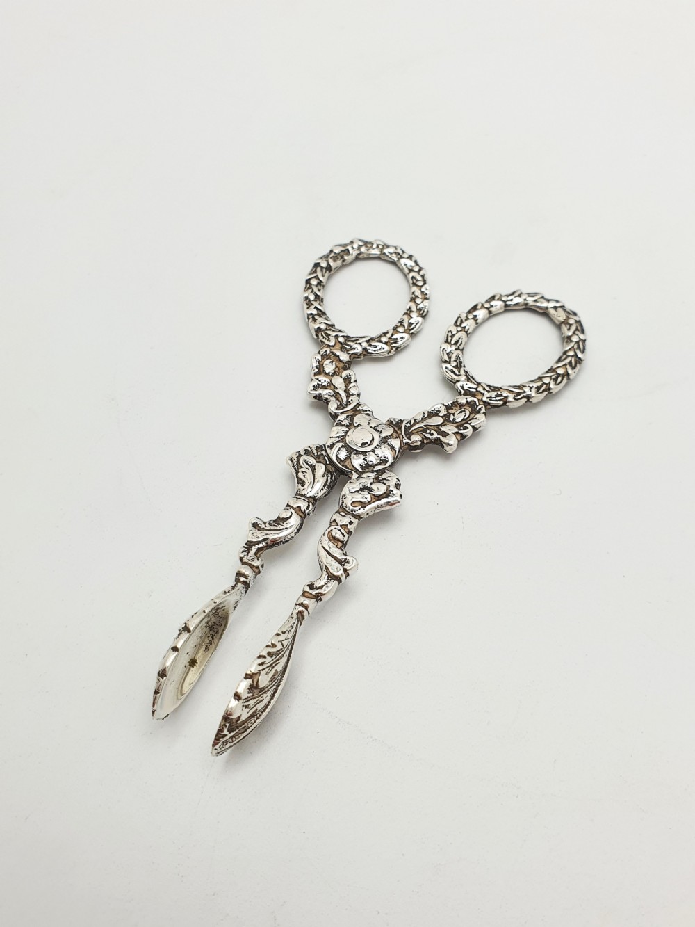 A pair of late Victorian sterling silver scissor-action sugar nips featuring floral relief motifs, round finger loops, and spoon-shaped tips.
