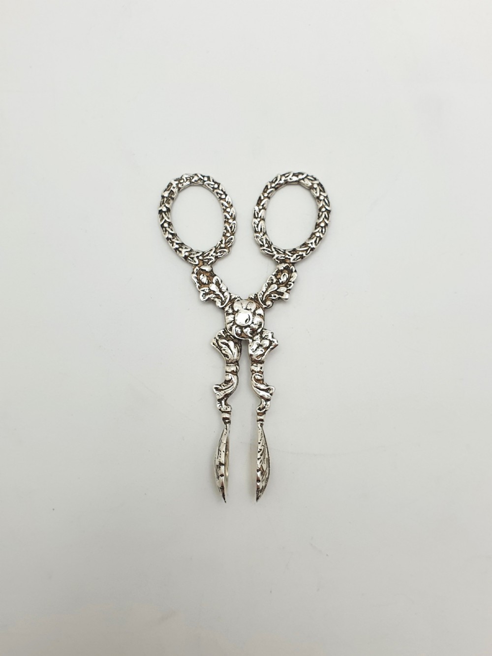 A pair of late Victorian sterling silver scissor-action sugar nips featuring floral relief motifs, round finger loops, and spoon-shaped tips. View II