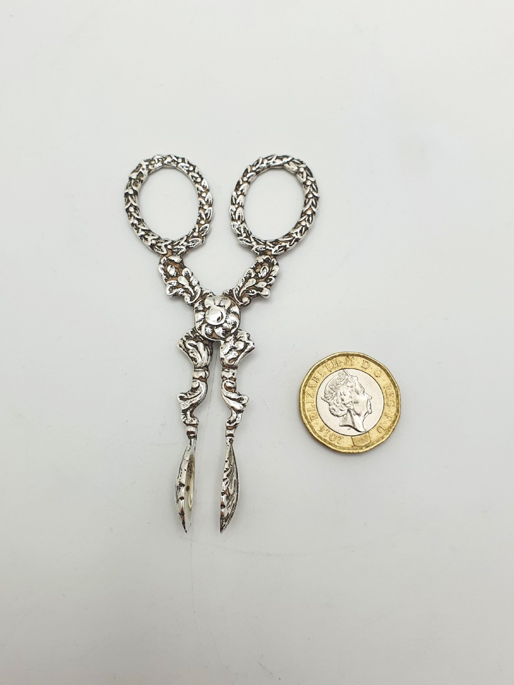 A pair of late Victorian sterling silver scissor-action sugar nips featuring floral relief motifs, round finger loops, and spoon-shaped tips. View VII