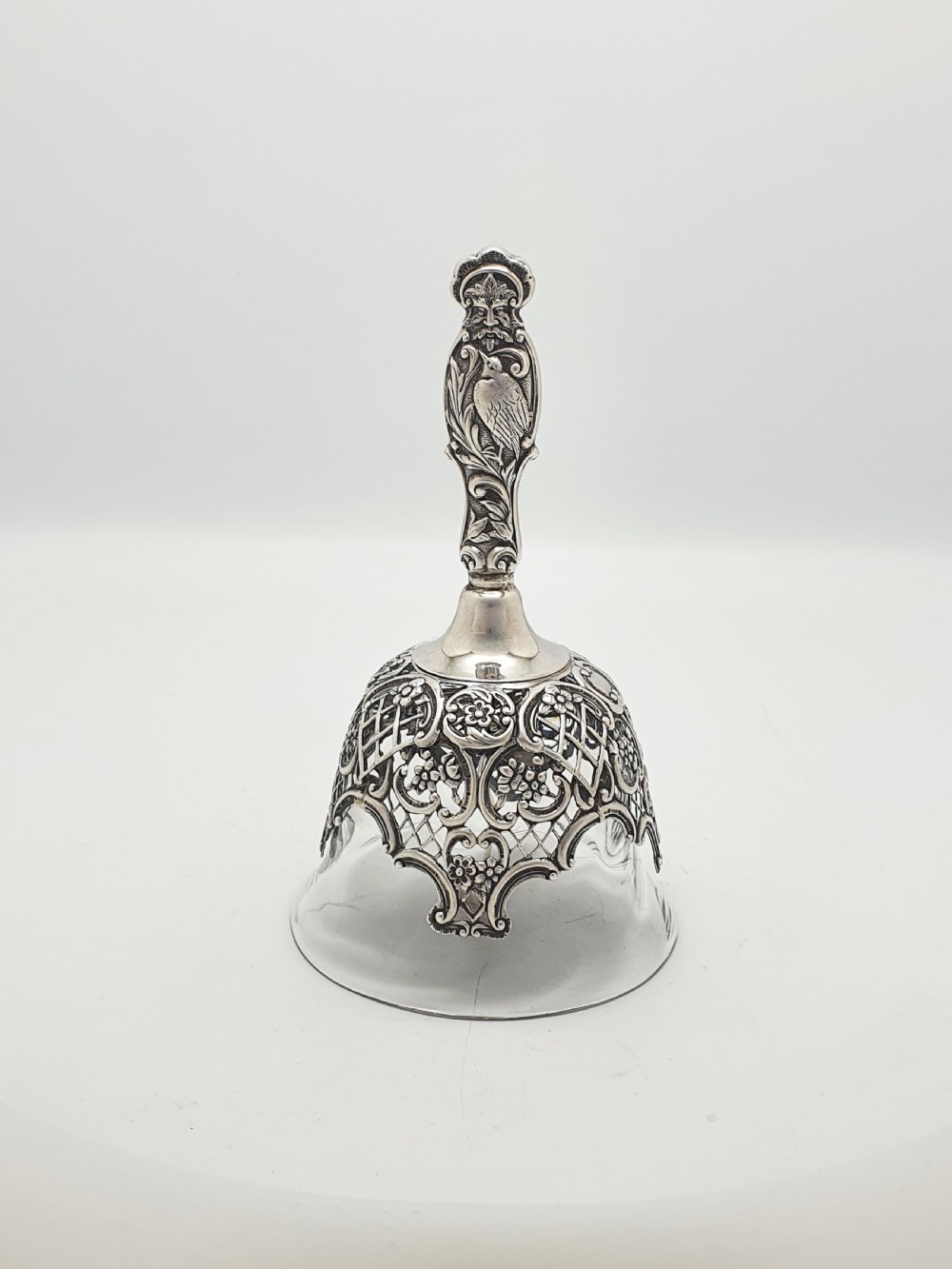 A late Victorian sterling silver and clear glass table bell with a figural handle and ornate pierced silver overlay.