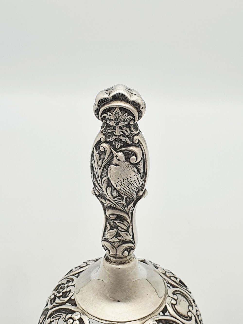 A late Victorian sterling silver and clear glass table bell with a figural handle and ornate pierced silver overlay. View II