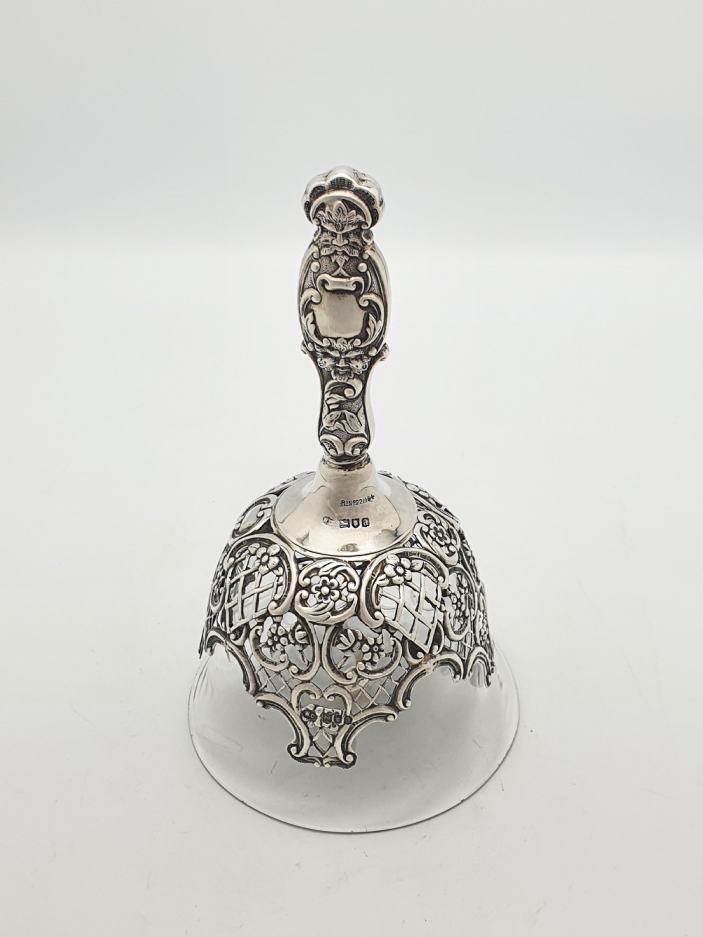 A late Victorian sterling silver and clear glass table bell with a figural handle and ornate pierced silver overlay. View V
