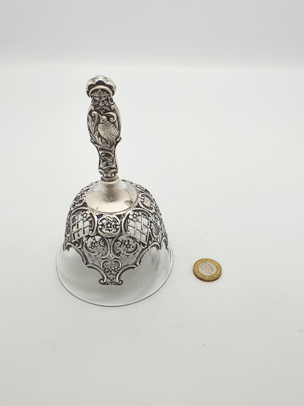 A late Victorian sterling silver and clear glass table bell with a figural handle and ornate pierced silver overlay. View IX