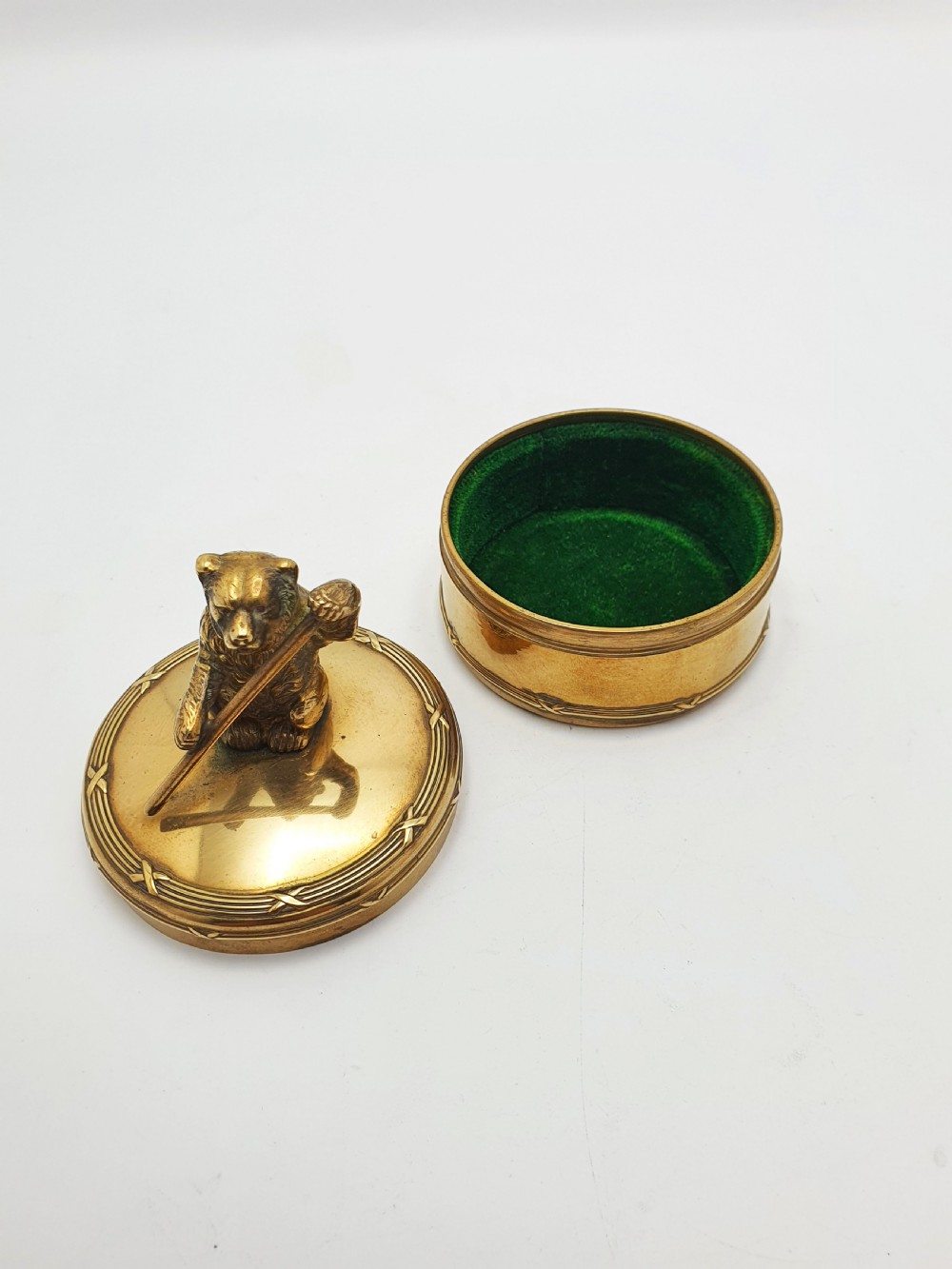 A small round brass trinket box featuring a detailed sculpted brass bear finial holding a stick on its lid. View VI