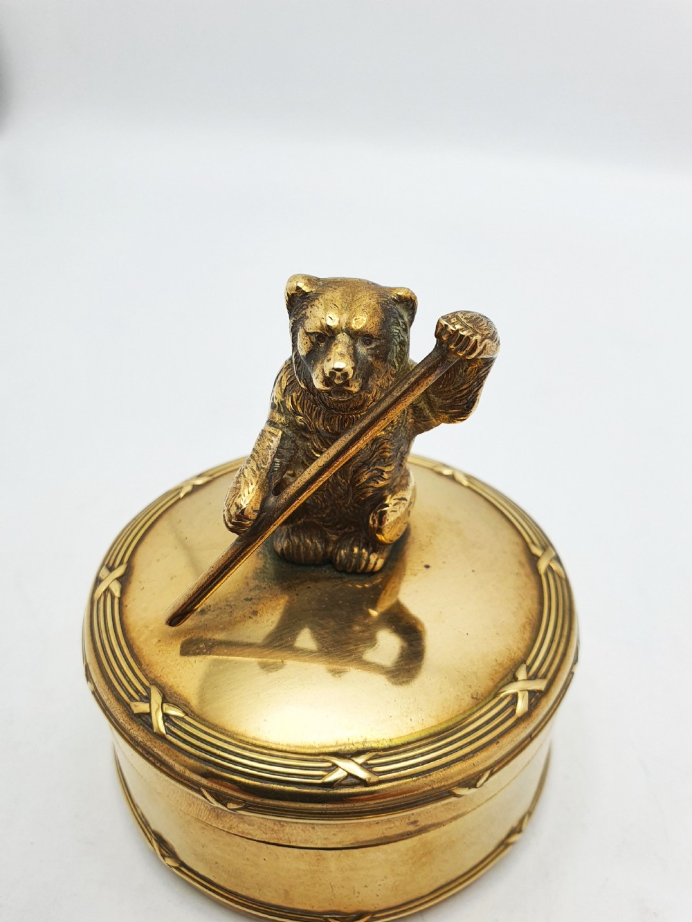 A small round brass trinket box featuring a detailed sculpted brass bear finial holding a stick on its lid. View VII