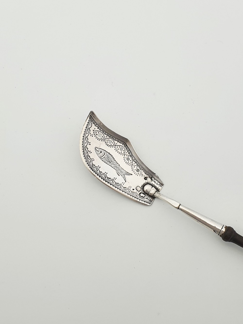 An antique silver sardine server featuring an engraved fish motif on a curved blade and a slender turned dark wooden handle. View II