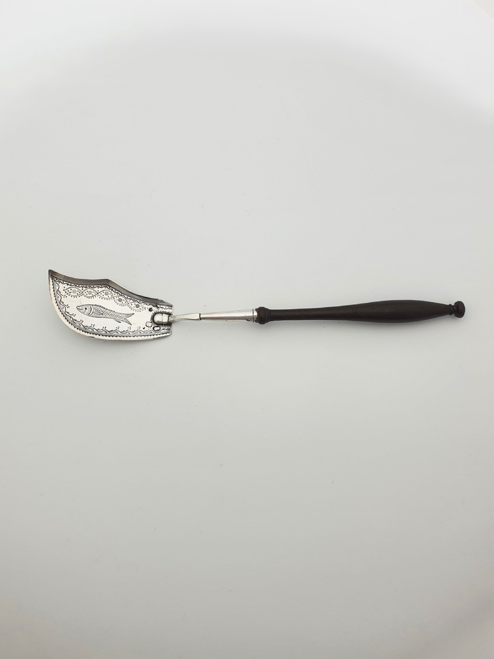 An antique silver sardine server featuring an engraved fish motif on a curved blade and a slender turned dark wooden handle. View VI