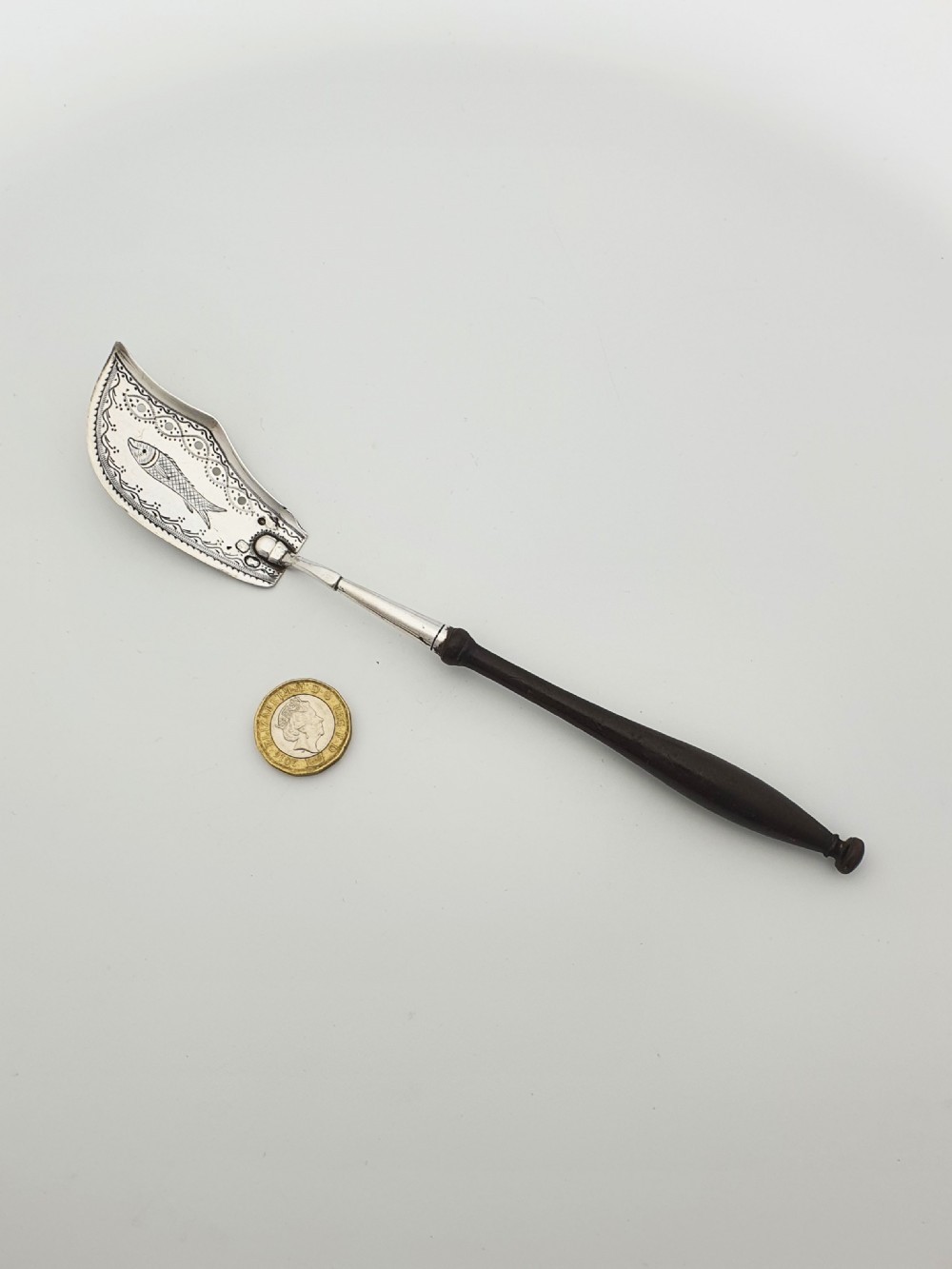 An antique silver sardine server featuring an engraved fish motif on a curved blade and a slender turned dark wooden handle. View VIII