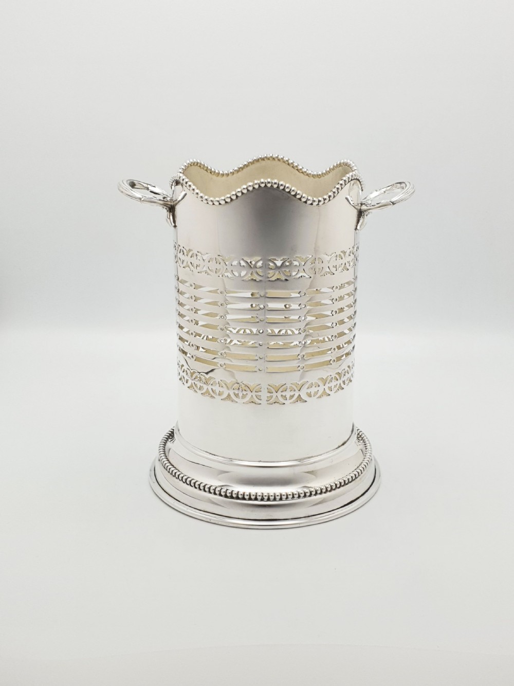 A cylindrical Edwardian silver-plated wine bottle coaster featuring pierced geometric fretwork, beaded rim detailing, a wavy scalloped rim, and two side handles. View II
