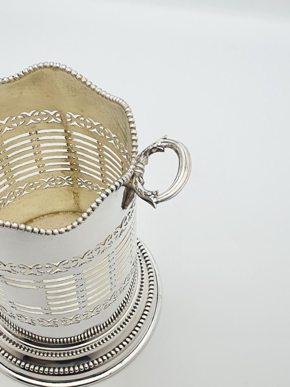 A cylindrical Edwardian silver-plated wine bottle coaster featuring pierced geometric fretwork, beaded rim detailing, a wavy scalloped rim, and two side handles. View III