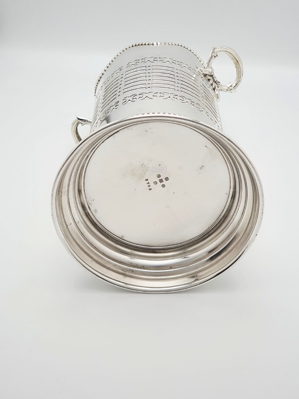 A cylindrical Edwardian silver-plated wine bottle coaster featuring pierced geometric fretwork, beaded rim detailing, a wavy scalloped rim, and two side handles. View V