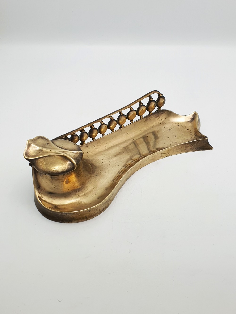 An Art Nouveau cast bronze inkwell featuring a hinged lid, organic curved pen rest tray, and decorative beaded back gallery.