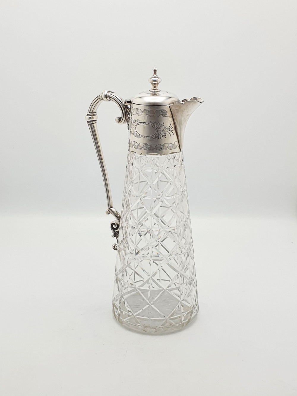 A Victorian conical cut-glass claret jug featuring a geometric diamond pattern with an engraved silver-plated neck collar, hinged lid, and decorative scroll handle. View III