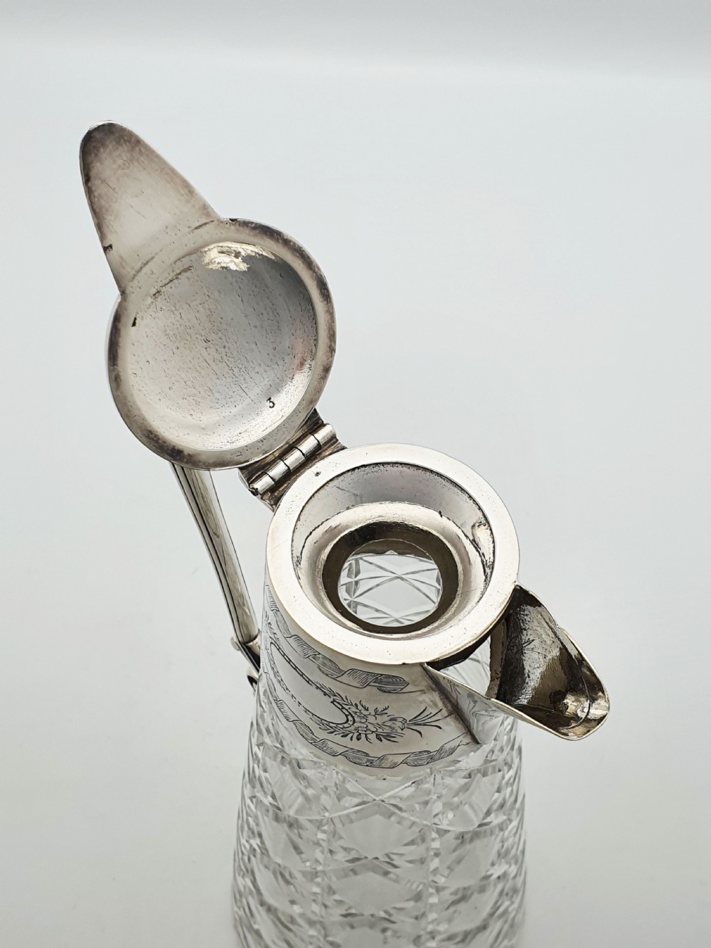 A Victorian conical cut-glass claret jug featuring a geometric diamond pattern with an engraved silver-plated neck collar, hinged lid, and decorative scroll handle. View VI