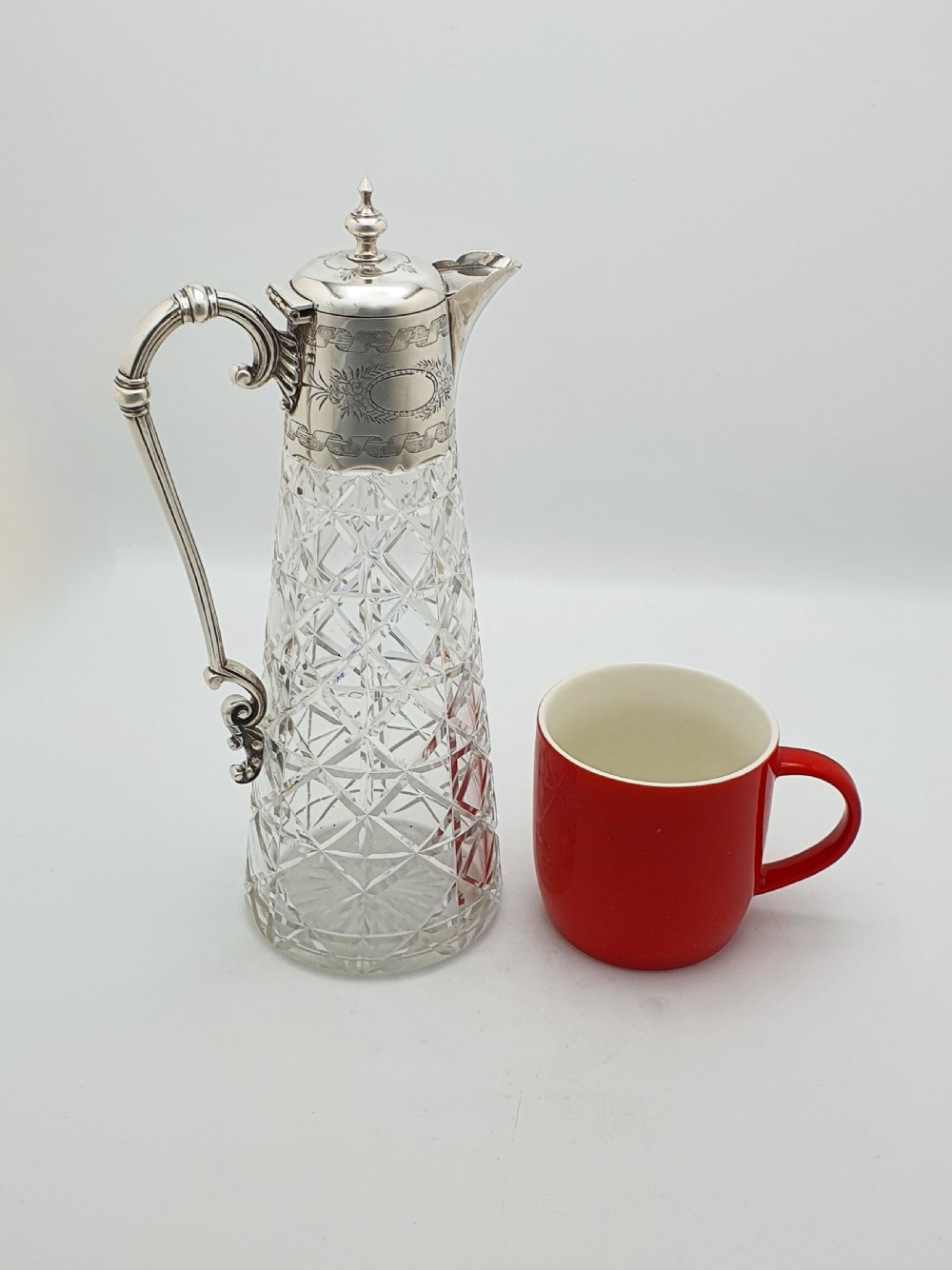 A Victorian conical cut-glass claret jug featuring a geometric diamond pattern with an engraved silver-plated neck collar, hinged lid, and decorative scroll handle. View VIII