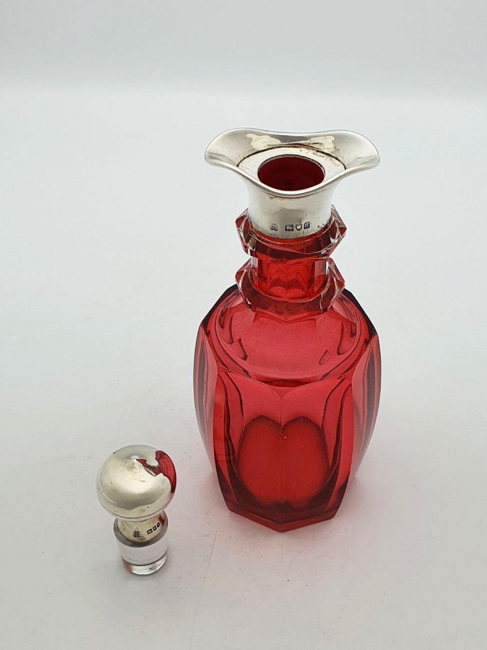 An Edwardian cranberry glass decanter featuring a faceted red body, a hallmarked sterling silver collar with a poured lip, and a matching silver stopper. View III